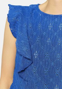 Zila teksturēta blūze ar apaļu kakla izgriezumu, volānu piedurknēm un dimanta rakstu ar izgriezumiem visā auduma virsmā.