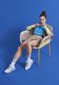 Lightweight, woven chair with multicolored accents; model wears a blue top, beige shorts, and white sneakers with black stripes on socks.