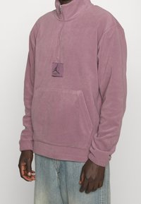 Fleece-pullov i ljuslila med halvdragkedja, framficka och Jordan-logotyp på bröstet. Mjuk textur och avslappnad passform.