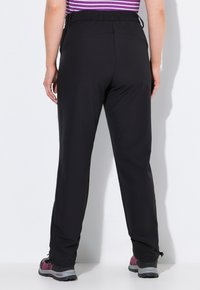 Zwarte hikingbroek met een strakke, elastische tailleband en een recht ontwerp. Gepaard met grijze en paarse wandelschoenen.
