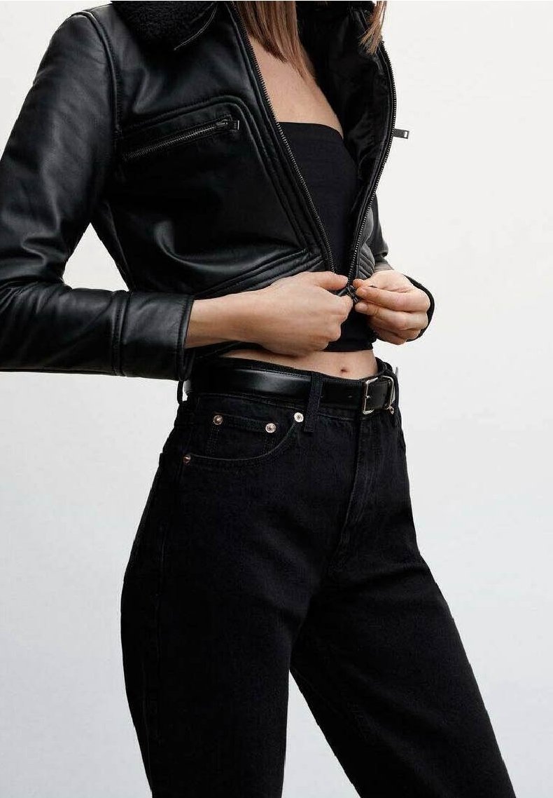 Personne portant une veste en cuir noire, un bustier noir et un jean noir taille haute en train de fermer la fermeture éclair de la veste.