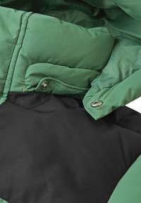 Giacca imbottita verde con un esterno liscio, dotata di una fodera interna nera, bottoni a pressione e dettagli di cucitura a contrasto.