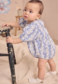 Világos színű babaruha kék virágmintákkal és rövid, puffos ujjakkal, deréknál ráncolt, fa gombos díszítéssel.