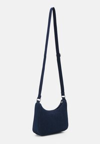 Granatowa torba na ramię z denimu o zaokrąglonym kształcie, regulowanym pasku i zamknięciu na zamek błyskawiczny. Charakteryzuje się gładką teksturą i minimalistycznymi akcesoriami.