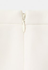 Primo piano di tessuto bianco con una cerniera centrata e una piccola linguetta di traino nella cucitura superiore.