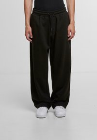 Black sweatpants made of soft fabric, featuring an elastic waistband, drawstring, and wide legs. Paired with white sneakers.