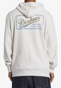 Light gray hoodie with a large blue and yellow "Dcshoes" graphic on the back, featuring ribbed cuffs and hem, made from a soft fabric.