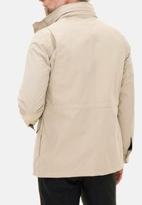 Beige vandtæt jakke med høj krave, glat tekstur og sidelommer. Viser bagview og et afslappet fit design.