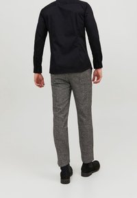 Svart långärmad skjorta i kombination med grå mönstrade byxor, som har en slim fit och slät tygkvalitet. Svarta stövlar fulländar looken.