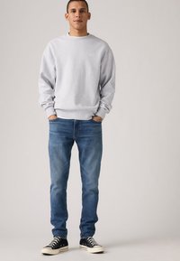 Sweatshirt cinza de gola redonda, jeans azul de denim e ténis pretos. Ajuste casual com punhos e barra canelados, textura lisa, sem padrões ou detalhes.