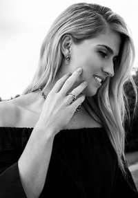 Zilveren creolen, een chunky ketting, en een ring. Model draagt een off-shoulder, zwarte, textuurtop, met lange, golvende haren.