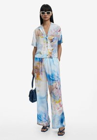 Twee-delige outfit met een kortbloedige overhemden en losse broek. Gemaakt van lichtgewicht stof met een blauw en meerkleurig abstract patroon.