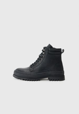 Black leather ankle boots with a rugged treaded sole, featuring round laces, metal eyelets, and a padded collar for added comfort.