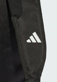 Tissu noir texturé avec un logo Adidas blanc proéminent comportant trois bandes diagonales. Bords renforcés et détails de couture visibles.