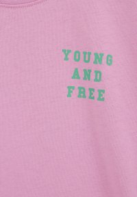 Vaaleanpunainen kangas, jossa vihreällä lihavoidulla tekstillä "YOUNG AND FREE" näkyvän alueen keskellä.