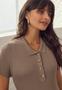 Linnen polo shirt in beige met ribbeltextuur, voorzien van een knoopsluiting en een klassieke kraag. Gouden creolen als accenten.