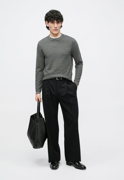 Adīta melna un balta rakstu džemperis ar apļveida kaklu, kombinēts ar augstās jostas melnām biksēm un lielu teksturētu melnu rokassomu.
