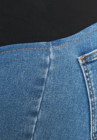 Svart tyg överlappar den övre kanten av blå denimjeans med synlig sömnad och en del av en bakficka på höger sida.