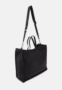 Schwarze Tragetasche mit weicher Textur, strukturiertem Design, dualen Obergriffen und einem verstellbaren Schulterriemen. Akzente aus silbernem Metall.