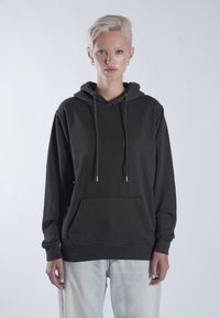 Fekete kapucnis pulóver zsinórral és kenguruzsebbel; puha anyagból készült, lazább fazonú, bordás mandzsettákkal. Világoskék farmernadrággal párosítva.