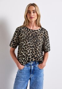 Top s krátkým rukávem v leopardím vzoru v béžové a černé barvě, s volným střihem a kulatým výstřihem, kombinovaný s modrými denimovými džíny.