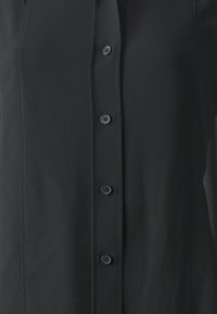 Black button-down shirt with a smooth texture, featuring six buttons and subtle stitching details along the seams.