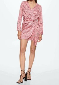 Robe portefeuille fleurie rose à manches longues, dotée d'un détail noué à la taille. Des sandales à talons noires avec des brides croisées complètent le look.