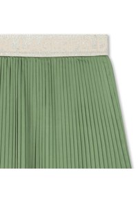 Πλισέ πράσινη φούστα με υφασμένο μπεζ ζωνάρι στη μέση, που φέρει το ανάγλυφο όνομα «KARL LAGERFELD», προσθέτοντας λεπτομέρεια και οπτικό ενδιαφέρον.