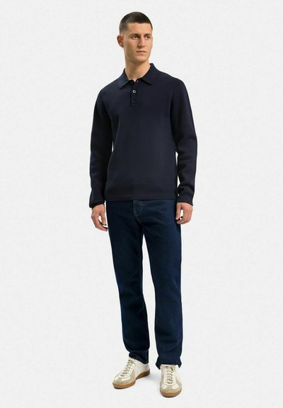 Marinblå tröja med krage, tre knappar, tillsammans med mörkblå jeans och vita sneakers med beige detaljer.