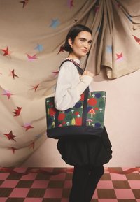 Kangaskassi, jonka taustaväri on vihreä ja jossa on värikkäitä sieni- ja pistekuvioita. Tummansinisiä yksityiskohtia ja vahvat olkahihnat.