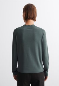 Grön tröja med långa ärmar, ribbad krage och fåll. Mjuk textur, minimala sömnadsdetaljer och standard passform. Synlig nacke bak.