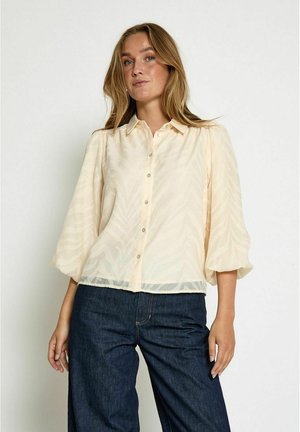 Light beige button-up blouse with a textured leaf pattern, soft fabric, and three-quarter sleeves, paired with dark blue denim pants.