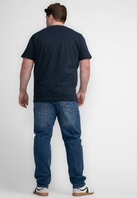 Camiseta de manga corta azul marino, de corte relajado, combinada con jeans de mezclilla azul claro; cuenta con bolsillos traseros y zapatillas blancas con acentos negros.