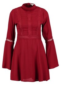 Robe rouge à manches longues avec des détails en dentelle sur le corsage, la taille et le haut des manches, avec un col montant et une jupe évasée.