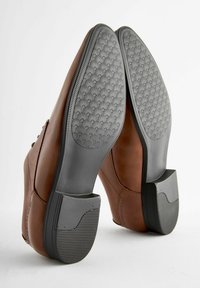 Brown leather shoes with rubber soles, featuring a textured grip pattern and a slight heel. Smooth finish with detailed stitching along the sides.