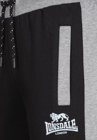 Svart och grå joggingsbyxor i en bomullsblandning, med dragsko i midjan, sidficka och en vit logotryck framtill.