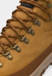 Κοντινό πλάνο καφέ βελούδινης πεζοπορικής μπότας με καφέ κορδόνια περασμένα μέσα από μεταλλικά οφθαλμάκια και ανθεκτική σόλα.