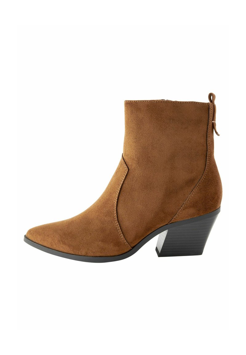 Stivaletto in suede marrone con punta affusolata, silhouette angolare e tacco impilato. Presenta una chiusura con zip e un linguetta sul retro.
