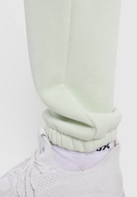 Ljusgröna sweatpants med elastiska muddar, gjorda av mjukt tyg, tillsammans med vita träningsskor och ett mönstrat vitt strumpa.