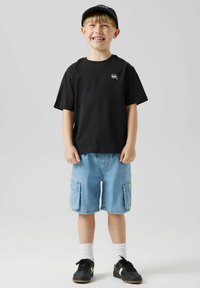 Čierne bavlnené tričko, svetlo modré cargo šortky s dvoma bočnými vreckami, čierne tenisky s bielymi akcentmi a biele krátke ponožky.