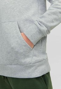 Sudadera gris claro con un acabado texturizado, con bolsillo canguro y puños acanalados, combinada con pantalones verde oscuro.