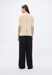 Top bej cu mâneci scurte, cu o cusătură centrală pe spate și detaliu cu fermoar, asortat cu pantaloni negri largi. Textură moale, design minimal.