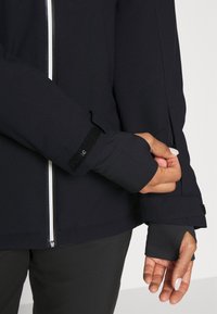 Giacca sportiva nera con zip frontale, aperture per il pollice, polsini in Velcro e tessuto elastico e liscio per un look aderente.