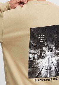 Beige sweater met ronde hals, voorzien van een vervaagd zwart-wit grafisch ontwerp van een stadsstraat, met de tekst "BLEND SINCE 1993" onderaan.