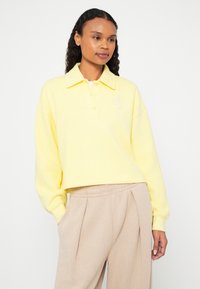 Žltá zúžená polokošeľa s dlhými rukávmi, vyrobená z textúrovanej tkaniny, so zapínaním na tri gombíky a malým vyšívaným logom.