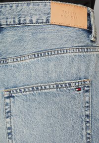 Lyseblå denimjeans med et lærmerke med "TOMMY HILFIGER" preget. Inkluderer en baklomme med en liten logodetalj.