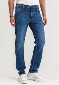 Niebieskie dżinsy o prostym kroju, z pięcioma kieszeniami, widocznym przeszyciem i zapięciem na guziki. Połączone z białymi trampkami.