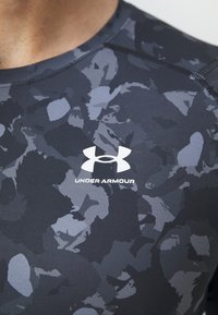 Meeste sobiv treeningpaita tumehallis värvuses, millel on kamuflaažimuster. Omab ümmargust kaelust ja valget Under Armour logo ees.