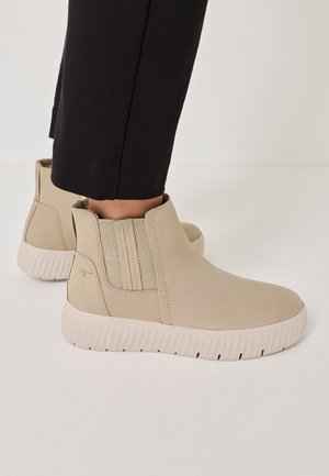 Beige ankle boots with elastic side panels and a textured rubber sole, featuring a smooth leather-like finish and minimalist design.