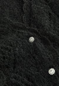 Tissu noir tricoté présentant deux boutons décoratifs en argent avec des pierres claires au centre disposés en motif floral.